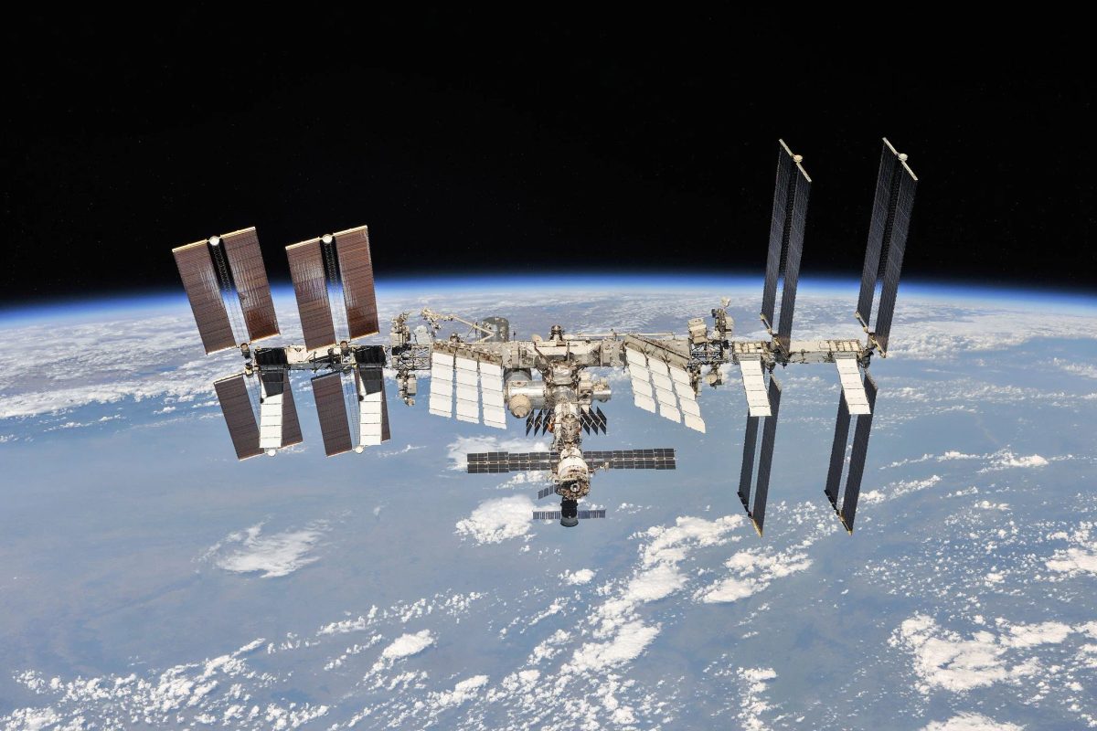 The International Space Station with its solar arrays extended, photographed in orbit above Earth's cloud-covered surface against the black of space