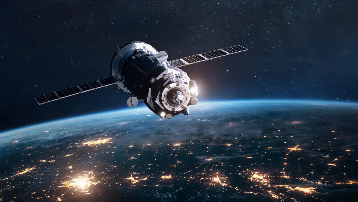 Spacecraft with extended solar panel arrays orbiting above Earth at night, with city lights glowing across the darkened surface below.